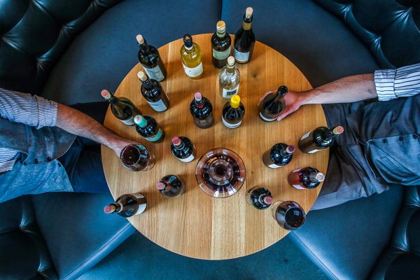 Table full of wine bottles with men\'s hands reaching out